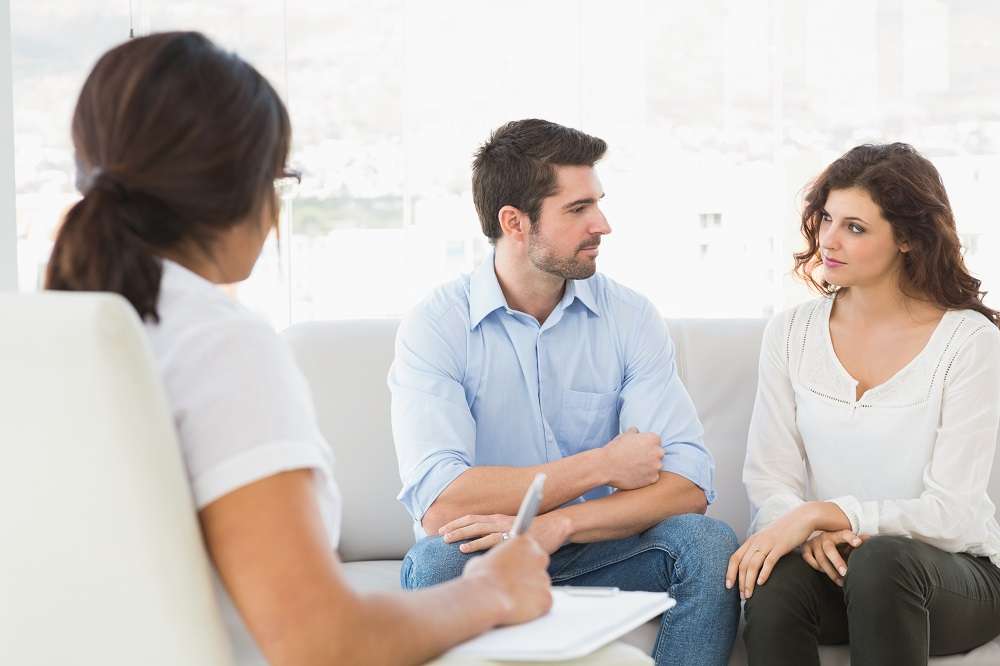Couple sitting on a sofa talking with their therapist
