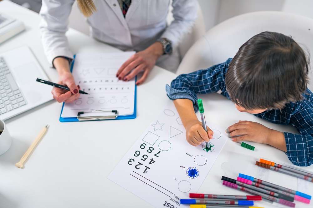 Child using a coloured pen to complete a test with a therapist