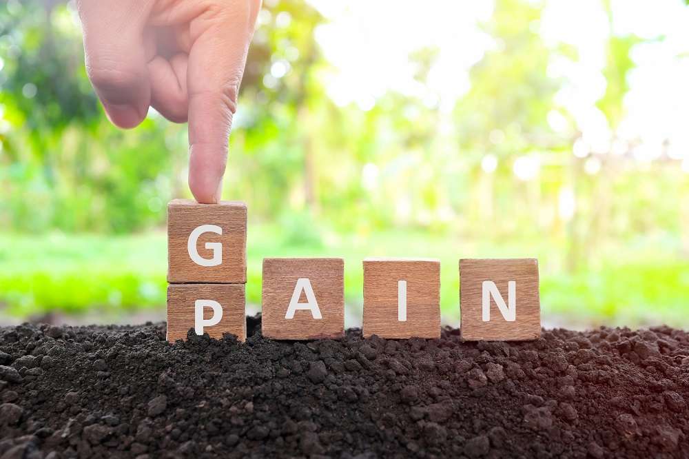 A hand is pushing down blocks that spell out the word Pain and replacing it with Gain