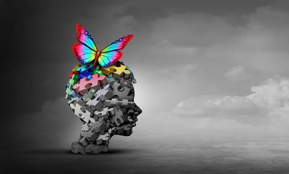 A human head made up of grey puzzle pieces with a colourful butterfly changing the puzzle pieces from grey to coloured