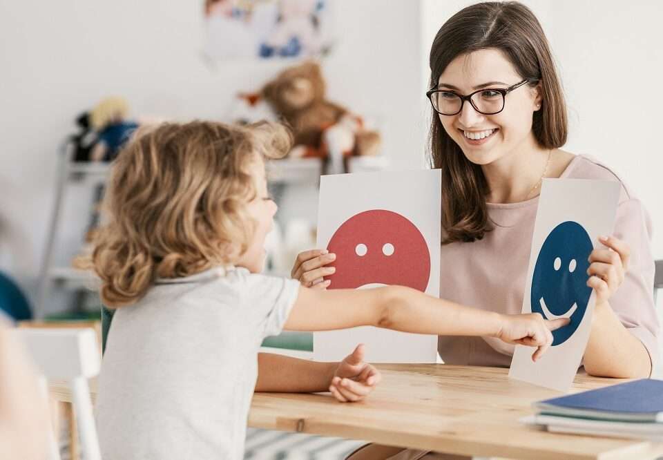 A female psychologist using emotion emoticons with a child during a therapy assessment