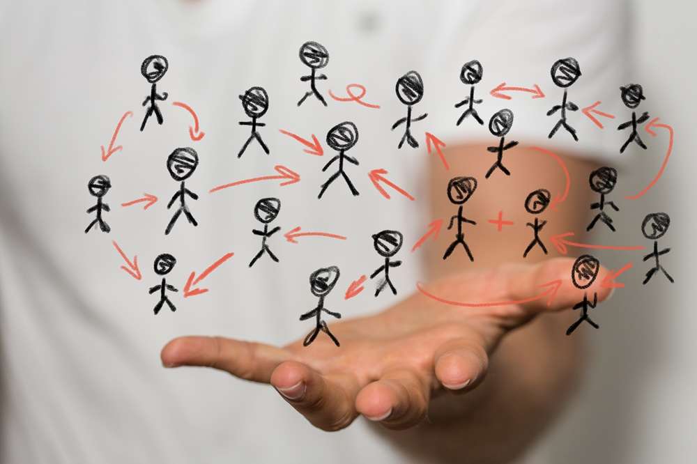 A human hand supporting a network of stick figure people connected by arrows