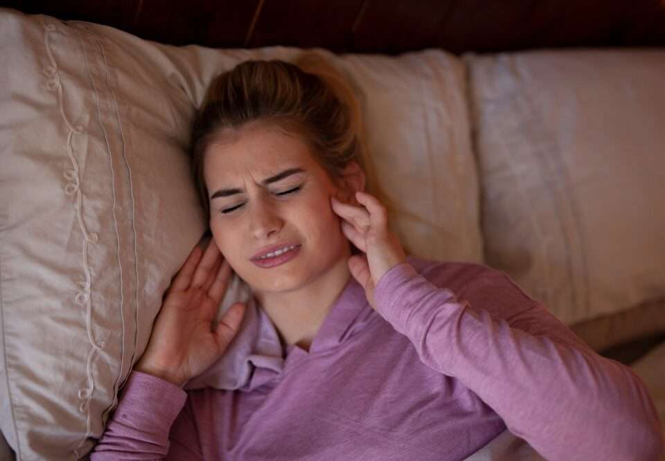 A woman lying in bed holding her jaw in pain with TMD