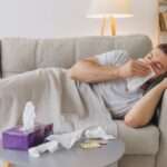 Man lying on a lounge blowing his nose and a table in front with tissues on it