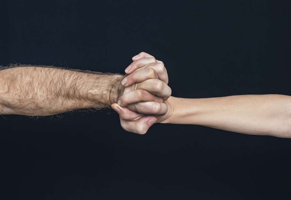 A male and female arm holding hands with intertwined fingers