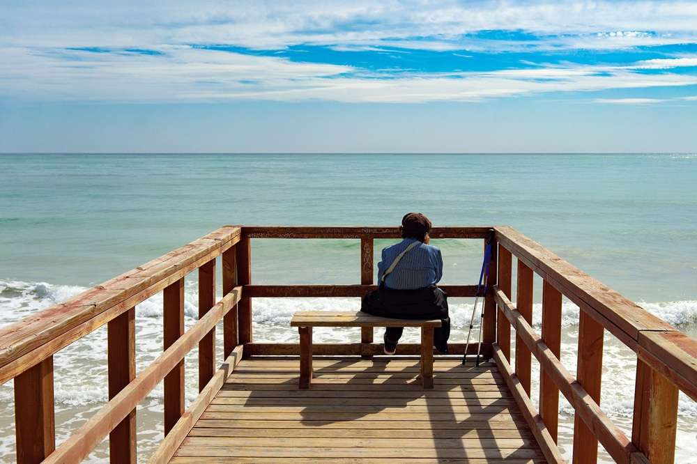A woman sitting on a seat at the end of a pier looking at the sea