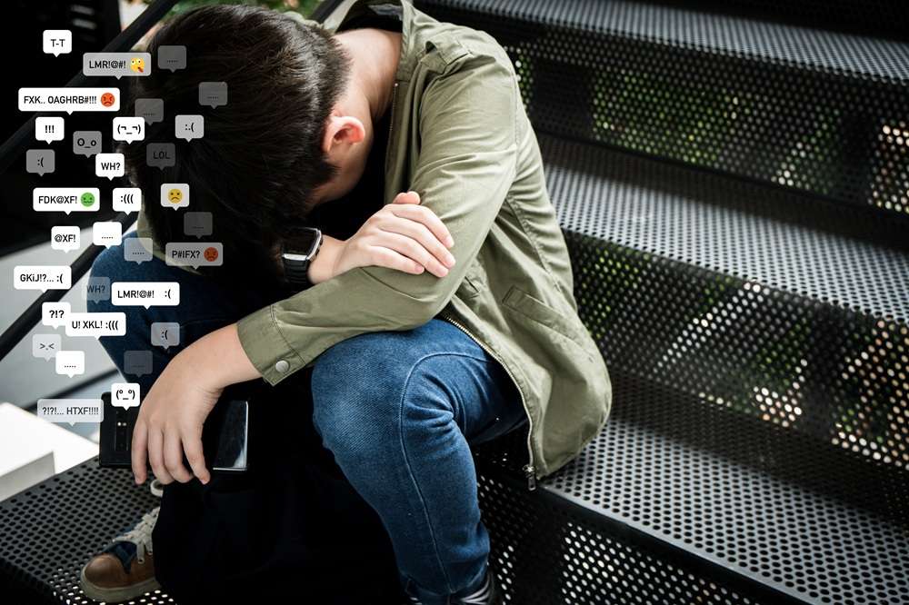 A depressed boy sitting on a step with cyberbullying social media messages