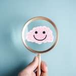 Inspecting the Brain - Paragon PsychConnect A magnifier held by a human hand focused over a cartoon human brain which is smiling