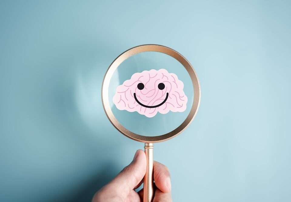 A magnifier held by a human hand focused over a cartoon human brain which is smiling