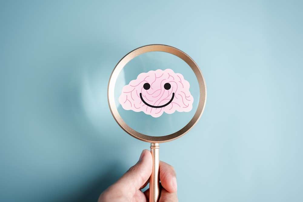 A magnifier held by a human hand focused over a cartoon human brain which is smiling