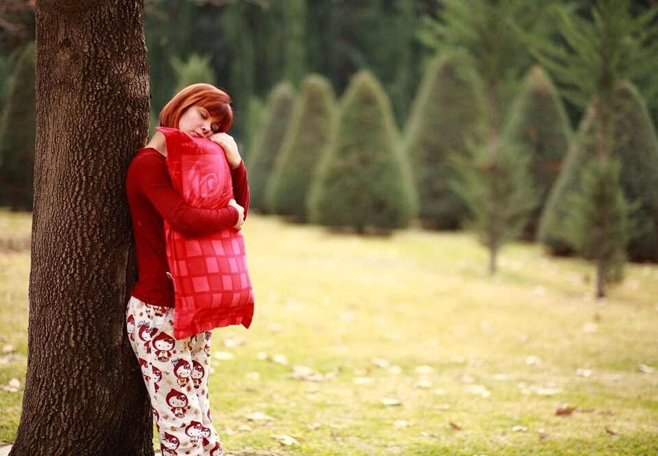 A woman holding a red pillow standing next to a tree