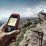 A human hand holding a GPS unit overlooking a scenic view