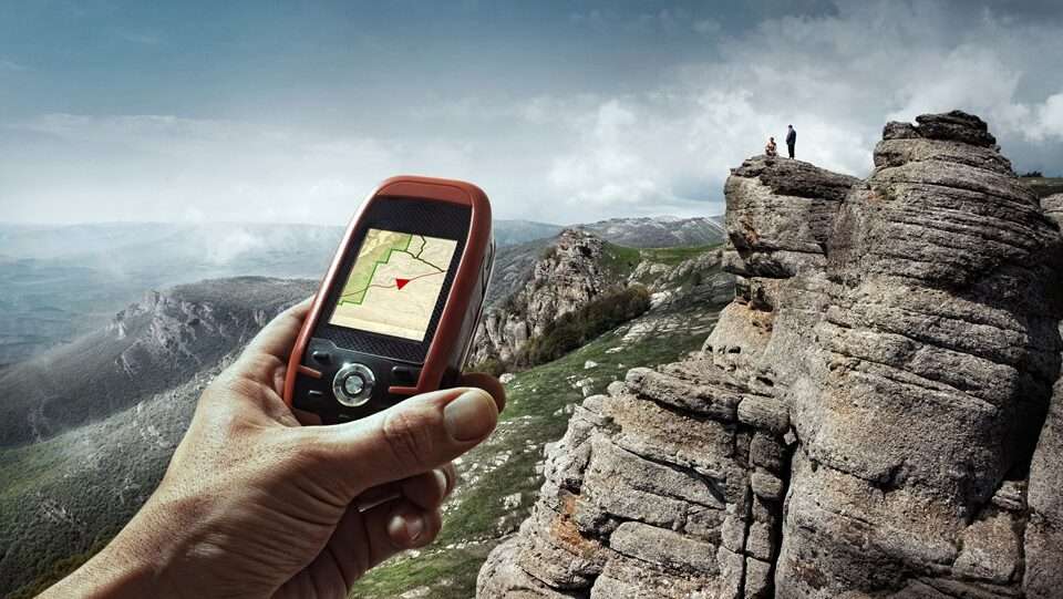 A human hand holding a GPS unit overlooking a scenic view