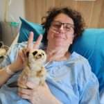 Maria lying in a hospital bed with Brucee the meerkat