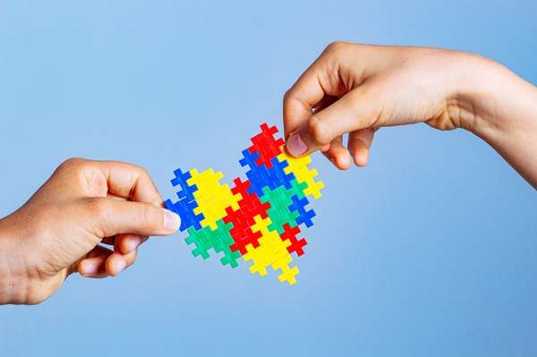 World Autism Awareness Day concept with two children's hands holding a colorful heart shaped puzzle