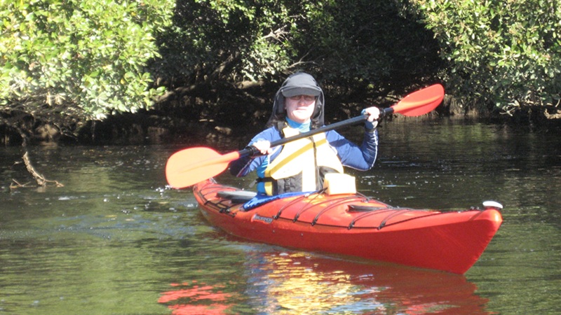 Maria paddling a red kayak on calm water at Torrens Island as she returns to valued activities after back surgery.